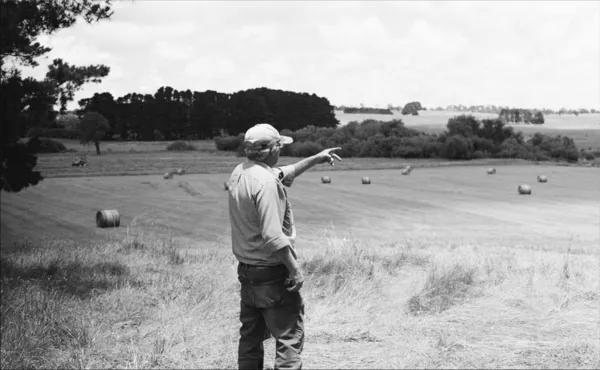 A farmer standing on a field, pointing off-screen.