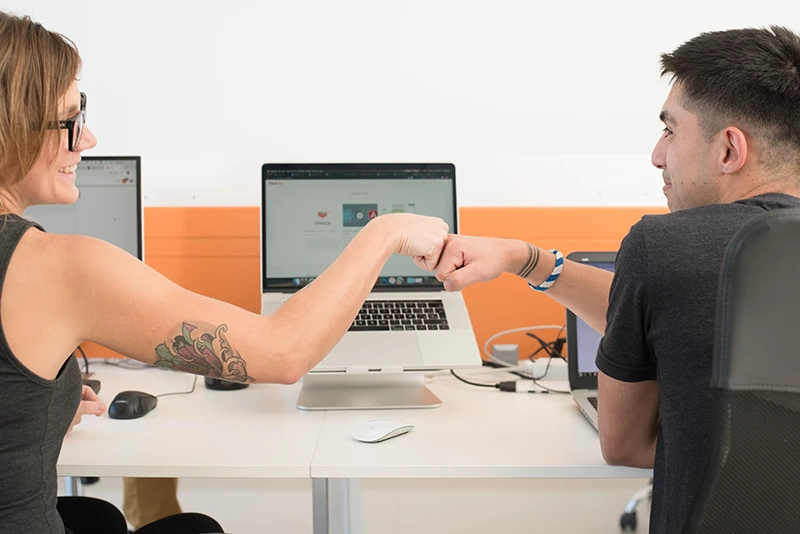 BeeReal employees bumping fists while working together at their computers.